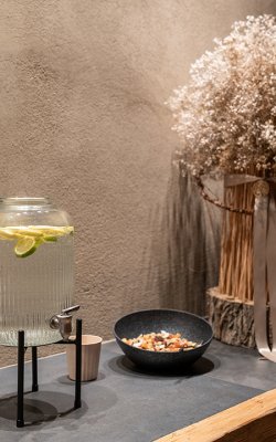 Glas mit Zitronenwasser auf Ständer neben Pappbechern, Schale mit Nüssen und Trockenblumen auf Holztisch