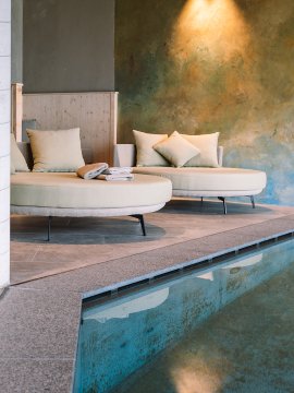 Due divani rotondi beige con cuscini accanto a una piscina e una parete illuminata