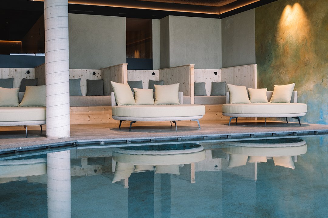 Moderne Lounge mit runden Sofas und Kissen neben einem Innenpool mit Säule