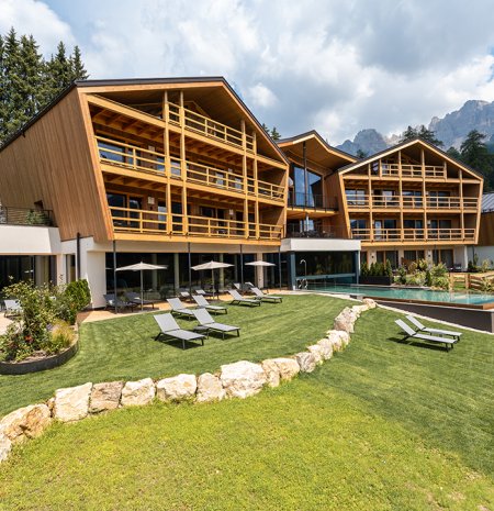 Modernes Holzgebäude mit Liegestühlen und Pool vor Bergkulisse unter bewölktem Himmel
