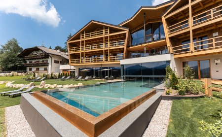 Edificio moderno in legno con piscina esterna e lettini su prato verde sotto cielo azzurro