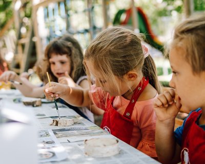 Bambini che dipingono all’aperto con pennelli e grembiuli rossi