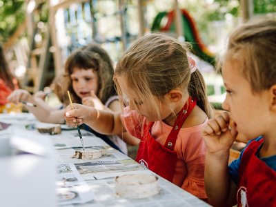 Children painting outdoors with brushes and red aprons