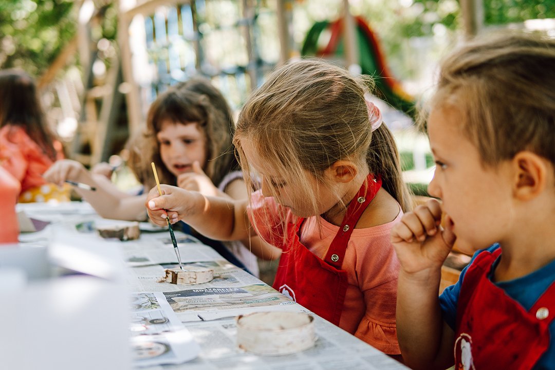 Kinder malen draußen mit Pinseln und roter Schürze