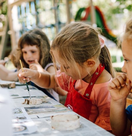 Kinder malen draußen mit Pinseln und roter Schürze