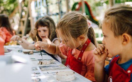 Kinder malen draußen mit Pinseln und roter Schürze