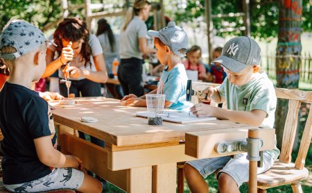 Kinder werkeln draußen an Holztisch mit Werkzeug