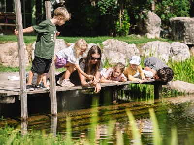 Kinder und eine Frau blicken von einem Steg auf einen Teich mit Fischen im Freien