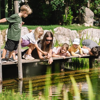 Bambini e una donna su un pontile che osservano i pesci in uno stagno all'aperto