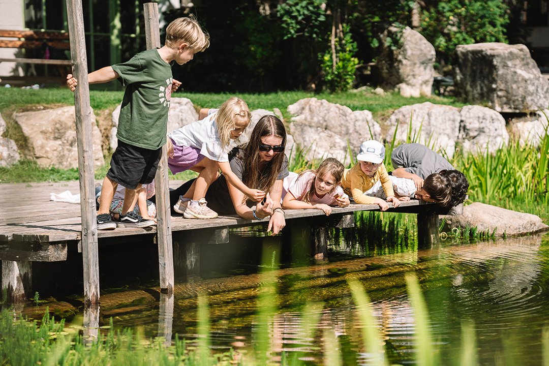 Kinder und eine Frau blicken von einem Steg auf einen Teich mit Fischen im Freien