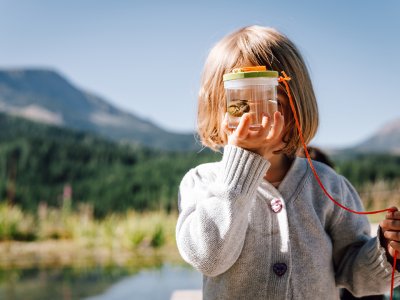 Bambino con lente e rana sullo sfondo di uno stagno