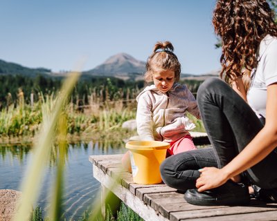 Bambina con secchiello su pontile di legno davanti a stagno e montagne