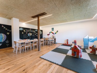 Kinderzimmer mit Tischen, Stühlen, Wandtafel mit Zeichnungen und Spielmatte mit Bauklötzen