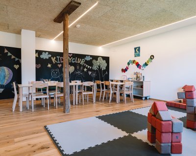 Kinderclubraum mit Holztischen, Stühlen, Wandtafelzeichnungen und Spielmatte mit Bauklötzen