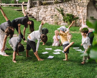 Kinder und Erwachsene machen Dehnübungen auf einer Wiese vor einer Steinmauer