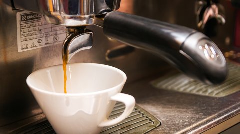 Kaffee fließt aus Maschine in weiße Tasse