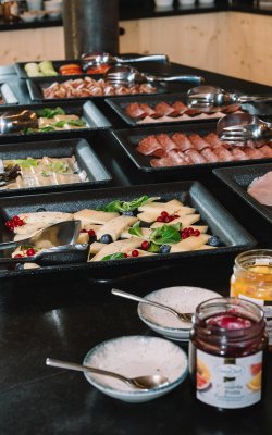 Buffet mit verschiedenen Käsesorten, Aufschnitt und Marmeladen in Gläsern auf schwarzem Tisch