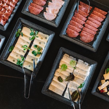 Verschiedene Wurst- und Käsesorten auf schwarzen rechteckigen Tellern mit Kräutern garniert
