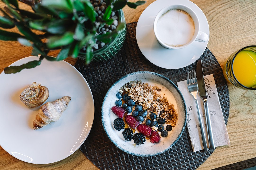 Frühstück mit Joghurt, Beeren, Müsli, Croissants, Kaffee und Orangensaft auf einem Holztisch