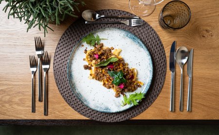 Oben auf einem Tisch angerichtete Pasta mit Hackfleisch und Kräutern auf einem weißen Teller mit blauem Rand