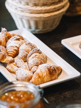 Tablett mit Croissants und Kuchenstücken, Gläser mit Marmelade im Vordergrund