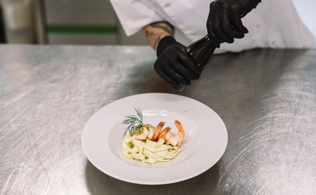 Chef seasoning pasta with shrimp in the kitchen