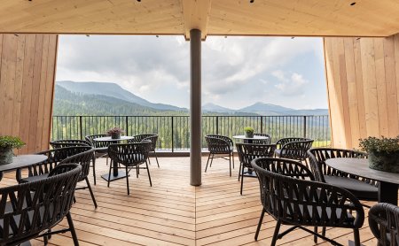 Überdachte Holzterrasse mit schwarzen Stühlen und Tischen, Blick auf bewaldete Berge