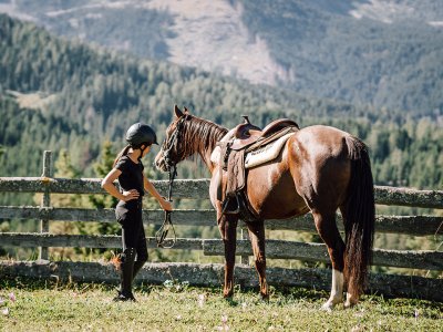 Mädchen mit Helm neben Pferd auf einer Almwiese