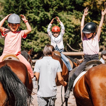 Kinder machen Gymnastikübungen auf Pferden mit Betreuung