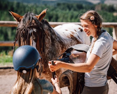 Reitlehrerin hilft Mädchen beim Nachziehen des Sattelgurts