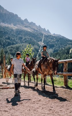 Kinder reiten mit Begleiter auf Reitweg vor steiler Bergkulisse