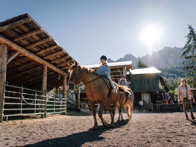 Kinder reiten Pferde im sonnigen Reitplatz vor Bergkulisse