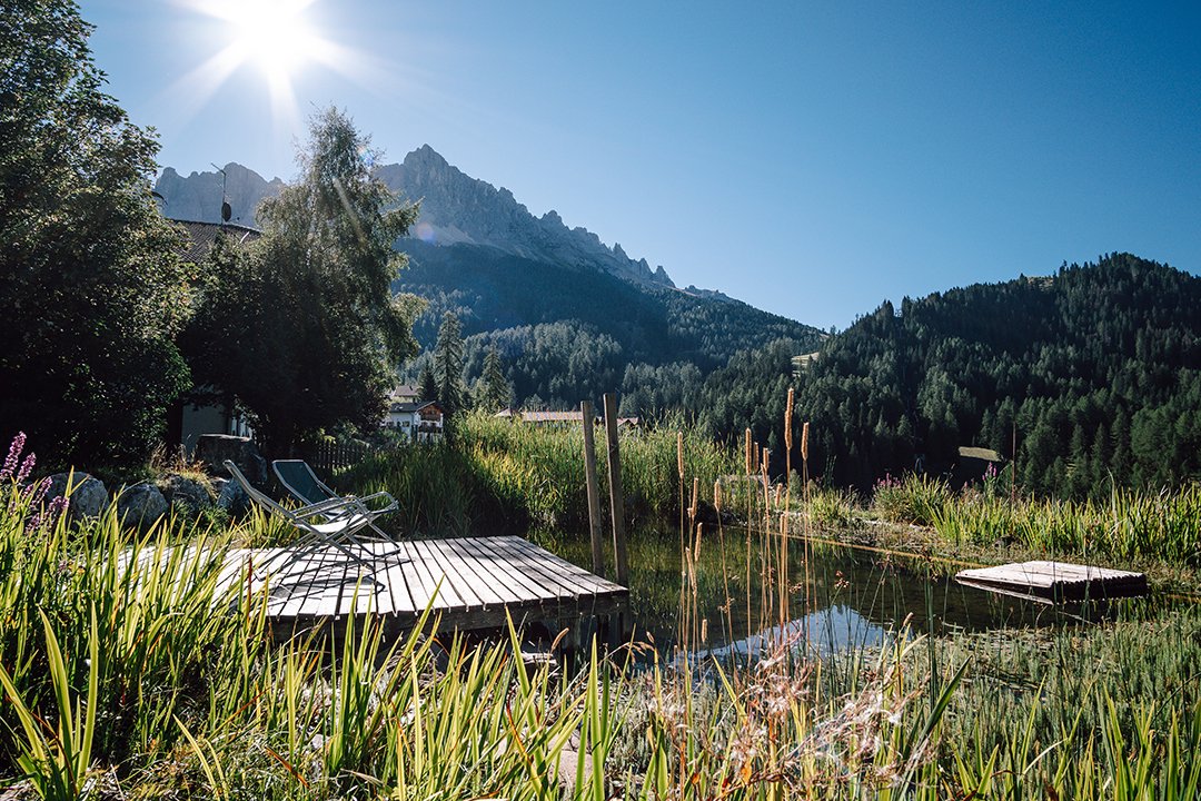 Steg mit Liegen am Naturteich vor sonniger Bergkulisse