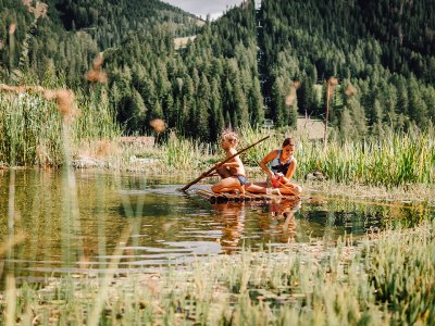Zwei Mädchen staken auf Holzfloß über Naturteich im Grünen