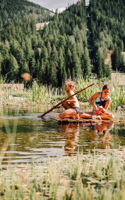 Zwei Mädchen staken auf Holzfloß über Naturteich im Grünen