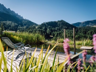 Zwei Liegestühle auf Holzsteg am Teich mit Bergpanorama