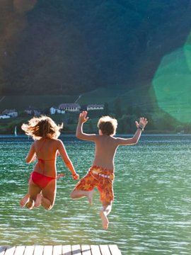 Kinder springen lachend von einem Steg in einen klaren See