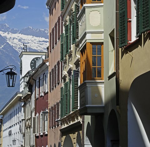 Altstadtgasse mit Uhrturm, bunten Fassaden und Blick auf Alpen