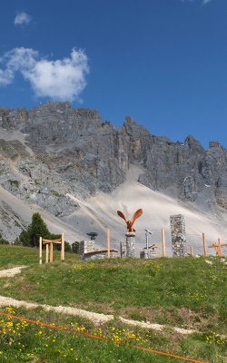 Adlerskulptur und Kreuze vor steiler Felswand in den Alpen