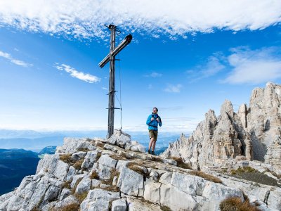 Wanderer steht am Gipfelkreuz mit Felsformationen im Hintergrund