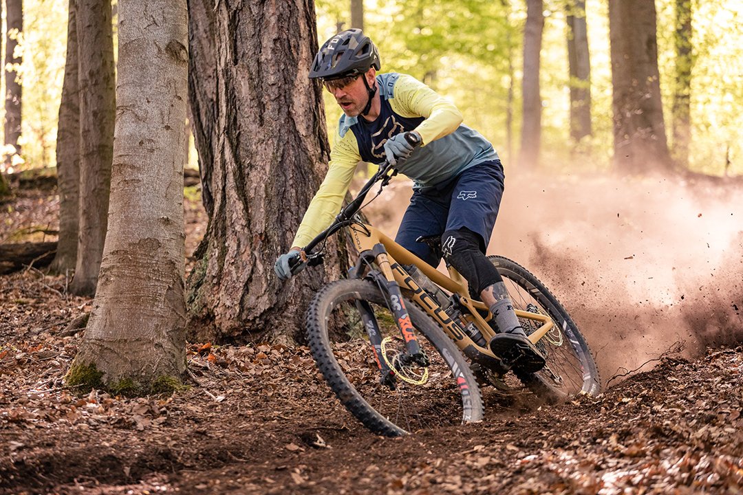 Mountainbiker driftet auf Waldboden zwischen Bäumen