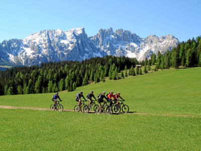 Gruppe Mountainbiker auf Wiese vor verschneiten Dolomiten
