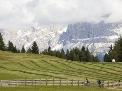 Zwei Mountainbiker vor Almwiese und verschneiten Dolomiten