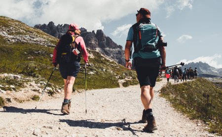 Wanderer mit Stöcken auf breitem Bergpfad in alpiner Landschaft