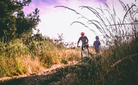 Kind und Erwachsener mit Helmen auf schmalem Naturweg im Gras