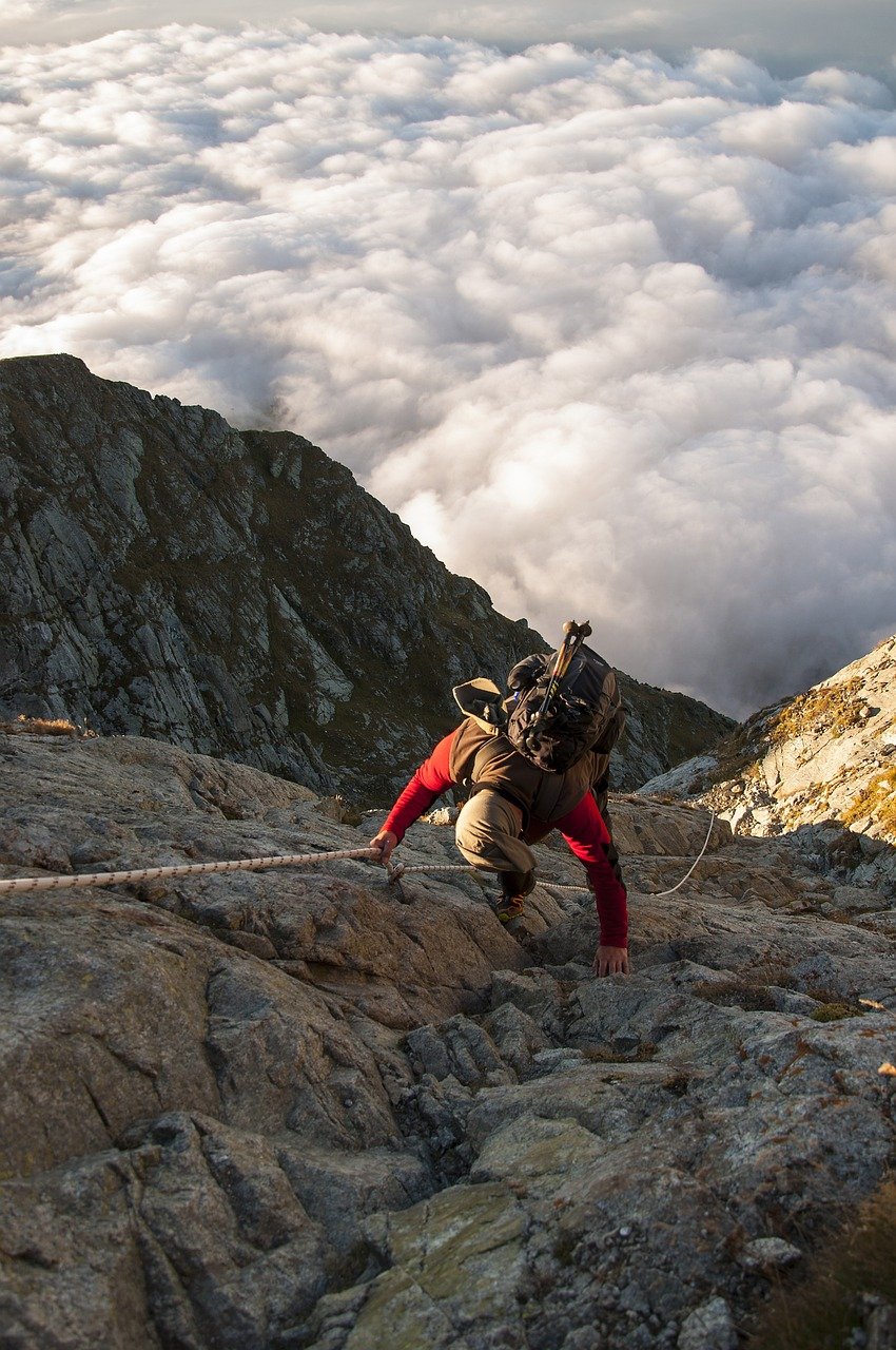 Kletterer zieht sich mit Seil über Felswand hoch, Wolkenmeer im Hintergrund