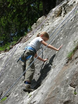 Mädchen klettert mit Klettergurt an natürlicher Felswand