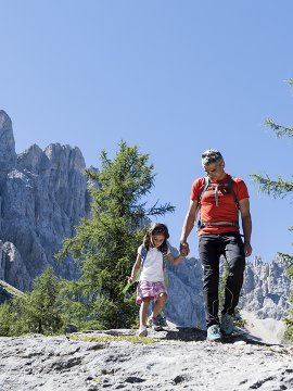 Mann und Kind wandern Hand in Hand vor Dolomitenfels