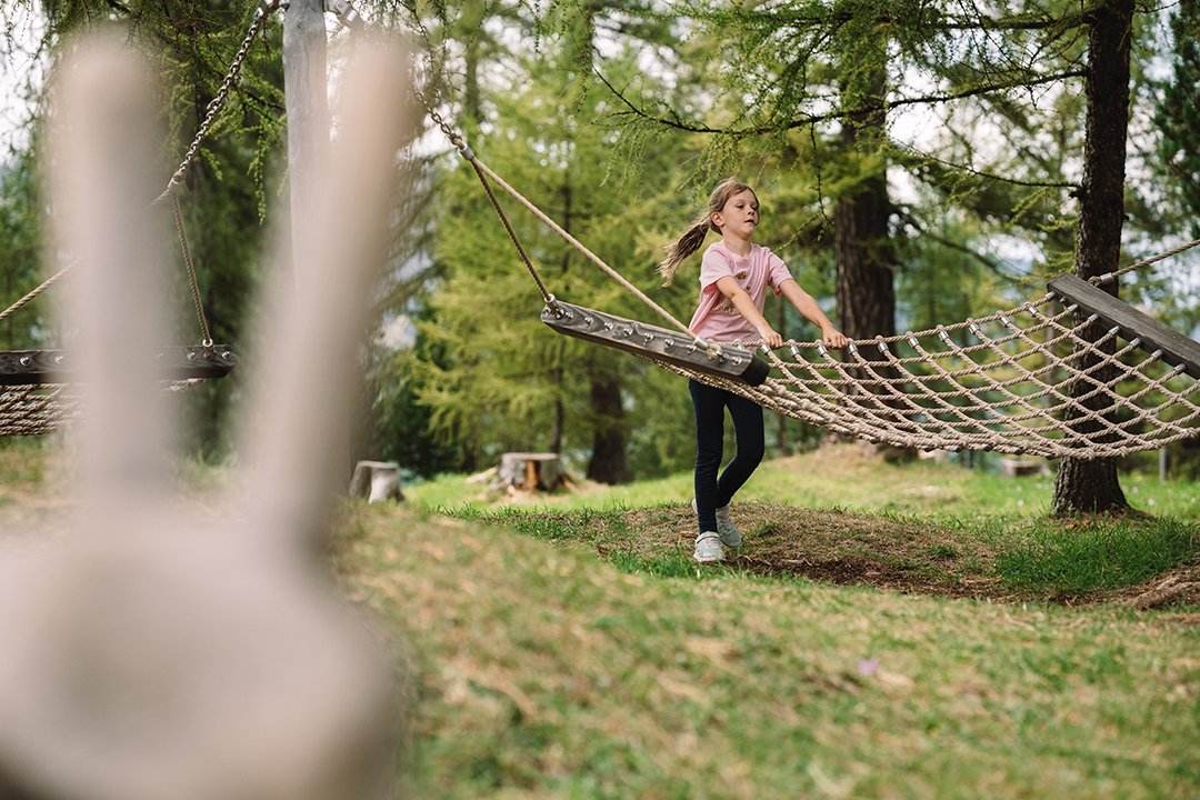 Girl in pink shirt stands next to a rope swing in a forest