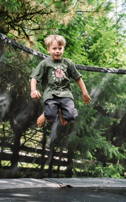 Boy jumping on a trampoline outdoors with trees in the background